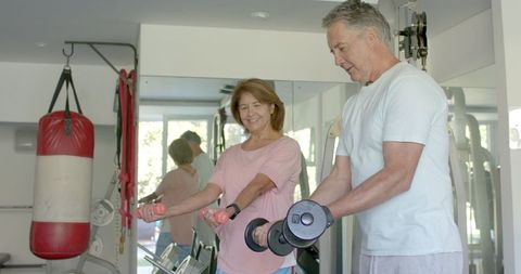 Senior couple exercising with dumbbells at home gym