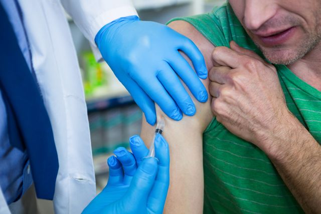 Pharmacist wearing blue gloves administering a vaccine injection to a patient's arm in a pharmacy. Useful for illustrating healthcare services, vaccination campaigns, medical procedures, and pharmacy-related content.