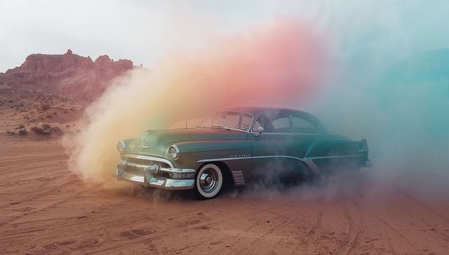 1950s classic sedan billowing pastel smoke on desert sand with chrome whitewall tires