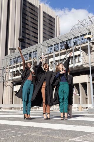 Diverse female graduates celebrating, tossing mortarboards, holding diplomas in urban plaza