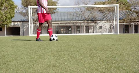 Soccer Player Dribbling Ball on Grass Field By Goalpost