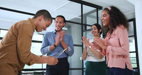 Diverse team celebrating employee achievement in modern office