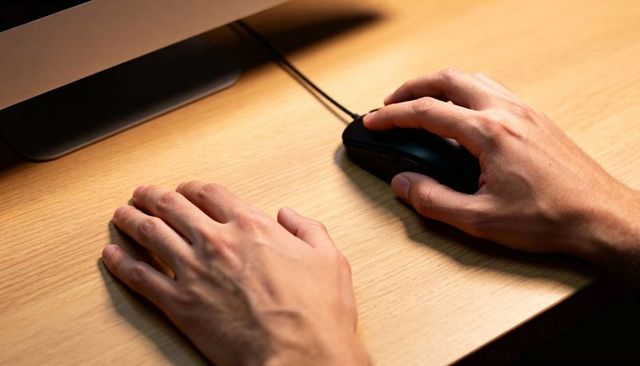 Gripping and resting hands using wired mouse on wooden desk with monitor base