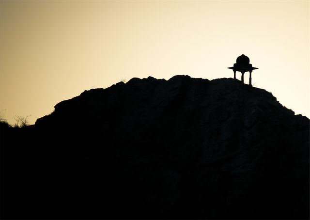 This image captures a solitary pavilion in silhouette atop a hill against a clear twilight sky. The scene conveys serenity and can be used for themes related to peace, nature, or solitude. It is suitable for backgrounds, travel brochures, meditation apps, and inspirational blogs.