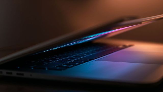 Slim aluminum laptop partially closing with ambient gradient lighting and glowing keyboard