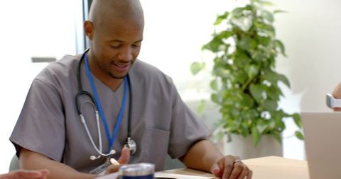 African american physician reviewing chart and writing at clinic table with stethoscope
