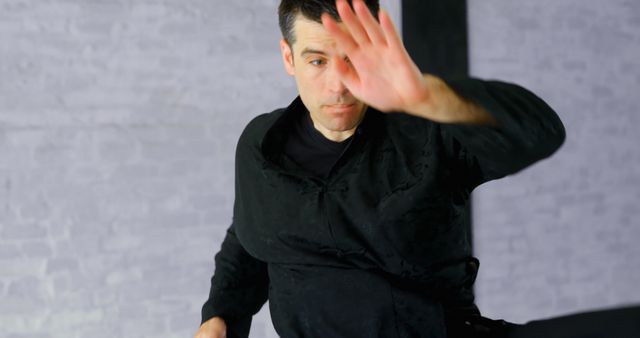 This image shows a man wearing a traditional martial arts outfit practicing indoors. He appears to be mid-action, displaying concentration and technique. This image can be used for themes related to martial arts, self-defense, physical training, discipline, and energy.