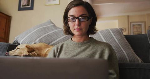 Woman in Glasses Focused on Laptop with Sleeping Dog beside Her