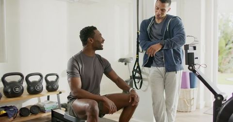 Personal trainer and client checking smartwatches in home gym with kettlebells, rowing erg