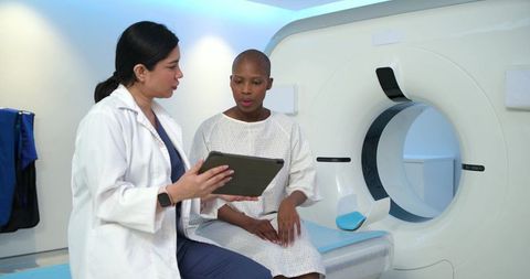 Female clinician consulting patient with tablet beside ct scanner in radiology suite
