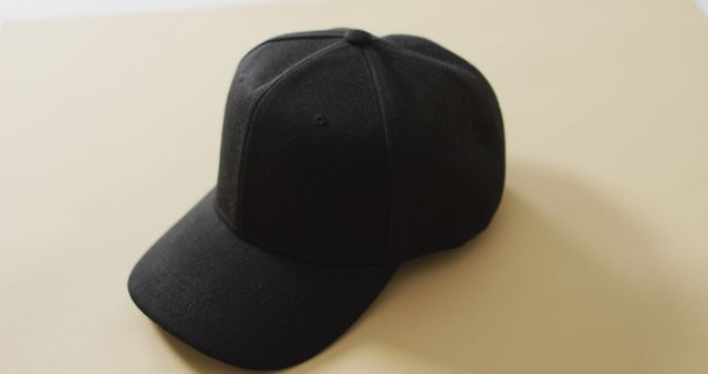 Plain black baseball cap placed on beige surface, suitable for fashion articles, accessory features, online clothing stores, and streetwear promotions. Ideal for minimalist design presentations.