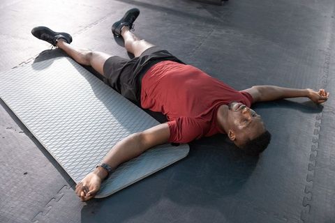 African american man lying on gym mat resting after workout wearing fitness tracker