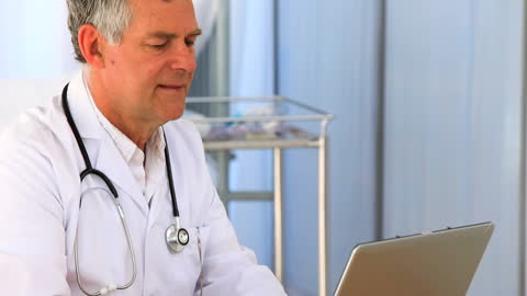 Senior Doctor Working on Laptop in Clinic Setting
