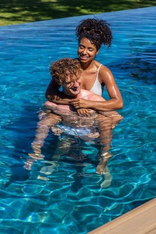 Interracial couple enjoying piggyback ride in sunlit pool laughing and splashing
