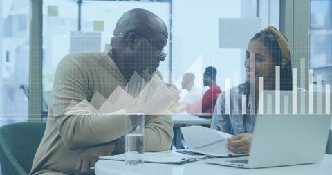 Senior professional mentoring colleague over laptop analyzing business charts and documents