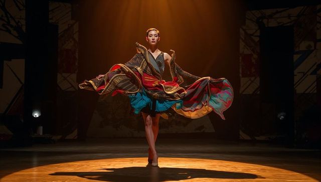 Asian dancer spinning under spotlight in flowing layered costume on theater stage
