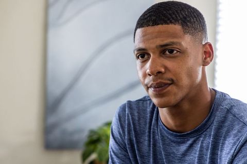 Thoughtful african american man wearing blue crewneck sitting indoors with soft natural light