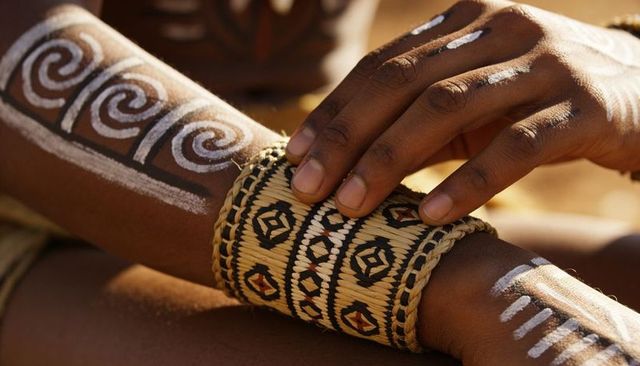 Adjusting woven cuff with geometric pattern and white spiral body paint on sunlit forearm