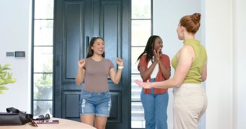 Diverse friends greeting at front door in bright modern foyer showing warm welcome