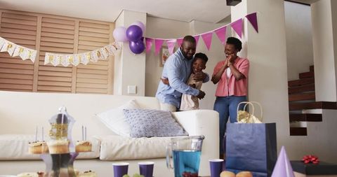 African American family celebrating birthday at home with purple decorations, cupcakes, gifts