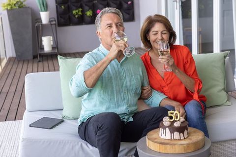 Senior couple celebrating 50th birthday on patio sipping wine with chocolate drip cake