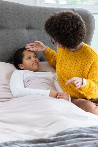 African american mother checking sick daughter in bed comforting and monitoring fever