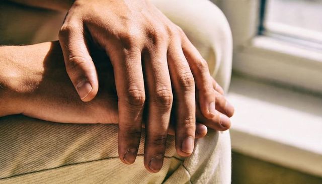 Resting adult male hands on knee in warm window light showing beige pants texture