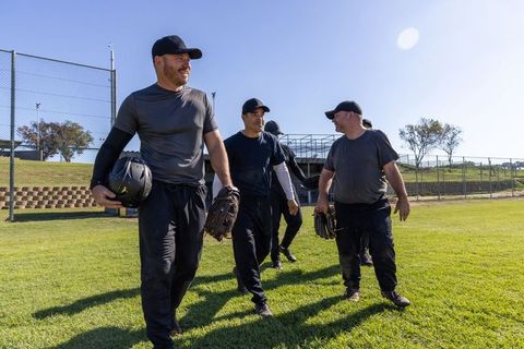 Sunlit adult baseball players walking off field after practice carrying gloves and helmet