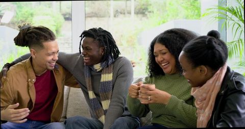 Multiracial Friends Laughing on Sofa Sharing Coffee and Stories in Bright Cozy Living Room