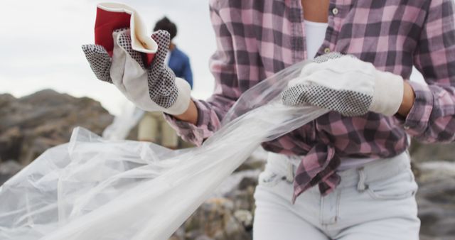 Group of environmental volunteers wearing gloves collecting plastic trash on a beach. Ideal for use in sustainability campaigns, environmental awareness programs, articles and blogs about ocean pollution and conservation efforts.