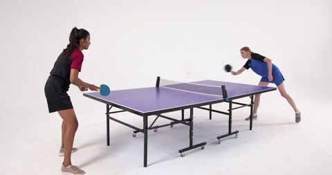 Female Athletes Playing Intense Ping Pong Match on Purple Table