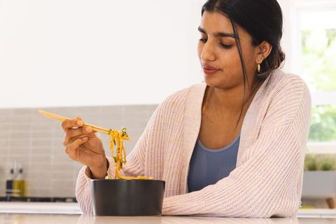 Woman Enjoying Noodle Meal with Chopsticks in Modern Kitchen
