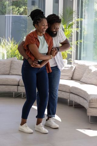 Laughing african american couple embracing in modern sunlit living room with curved sofa