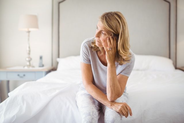 Tensed woman sitting on bed in bedroom at home