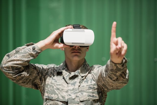Military soldier in camouflage uniform using virtual reality headset, pointing forward. Ideal for illustrating modern military training, technology in defense, and innovative simulation techniques. Useful for articles on military technology, VR applications in training, and advancements in defense strategies.