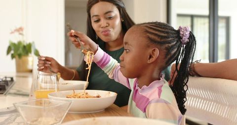 African american family sharing spaghetti at kitchen island, mother and daughter bonding