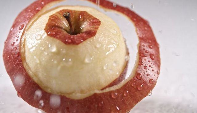 Rinsing peeled red apple with spiral peel and water droplets, macro studio closeup