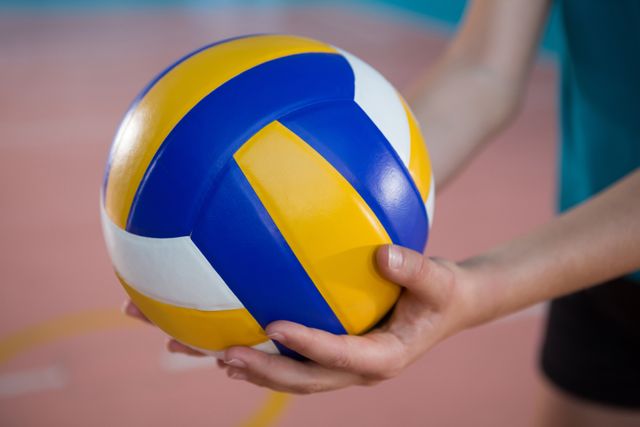 Close-up of female player holding volleyball in court. Ideal for sports-related content, fitness blogs, team sport promotions, and athletic training materials.