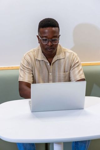 Focused african man working on laptop in minimalist casual workspace with neutral tones