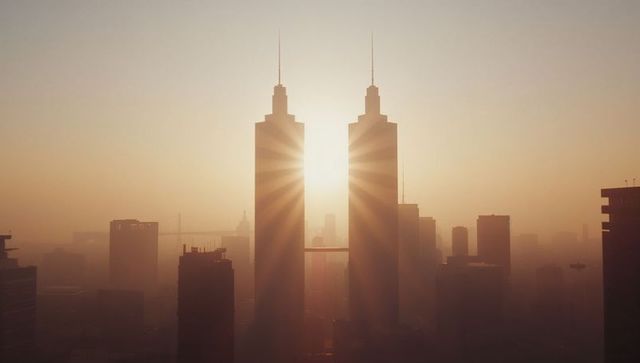 Twin skyscrapers illuminated by sunrise through hazy urban cityscape