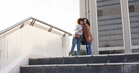 Two women hugging on urban stairs with crossbody bags embracing friendship and chic style