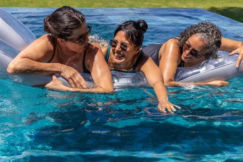 Mature women enjoying silver pool float together laughing and relaxing in backyard summer