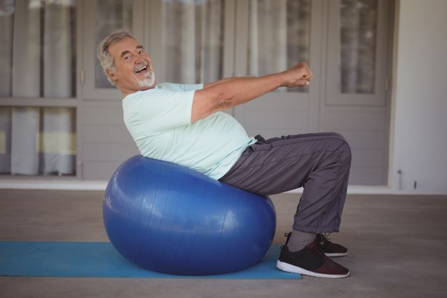 Senior man smiling while doing stretching exercises on a stability ball outdoors. Ideal for promoting senior fitness, healthy lifestyle, and active aging. Suitable for use in health and wellness articles, fitness blogs, and advertisements targeting elderly fitness programs.