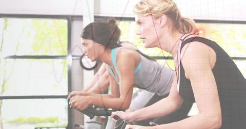 Blonde woman leading intense indoor cycling spin class on bike with red earphones