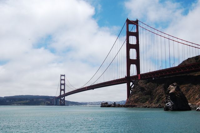 Showcasing the iconic Golden Gate Bridge stretching across the bay with a backdrop of blue sky and partial clouds. Ideal for travel guides, brochures, educational materials on civil engineering and architecture, tourism promotion, and social media posts celebrating famous landmarks.