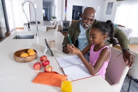 African american grandfather helping granddaughter with homework on tablet in kitchen