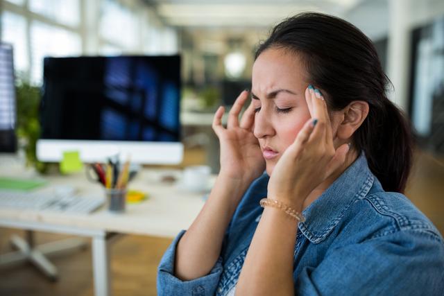 Female graphic designer suffering from head pain in office