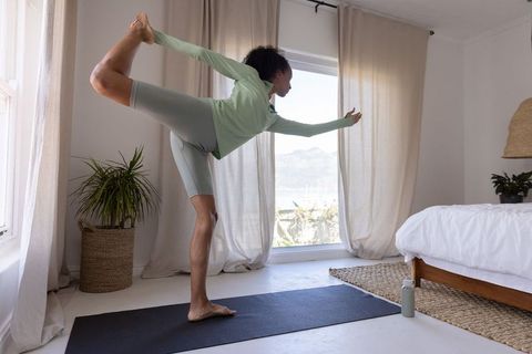 African american woman practicing yoga dancer pose in sunlit bedroom with coastal view