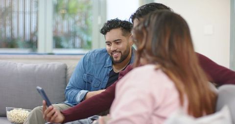 Friends Watching Smartphone and Sharing Popcorn on Sofa in Casual Living Room