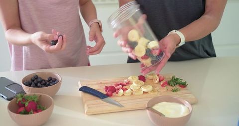 Diverse couple preparing fruit smoothies together on bright kitchen counter